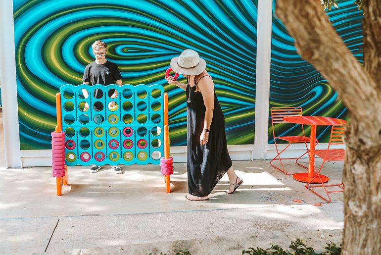 7 Great Reasons You Should Visit San Antonio With Your Family Woman and son playing large connect 4 game in front of blue and green wall at a park in San Antonio